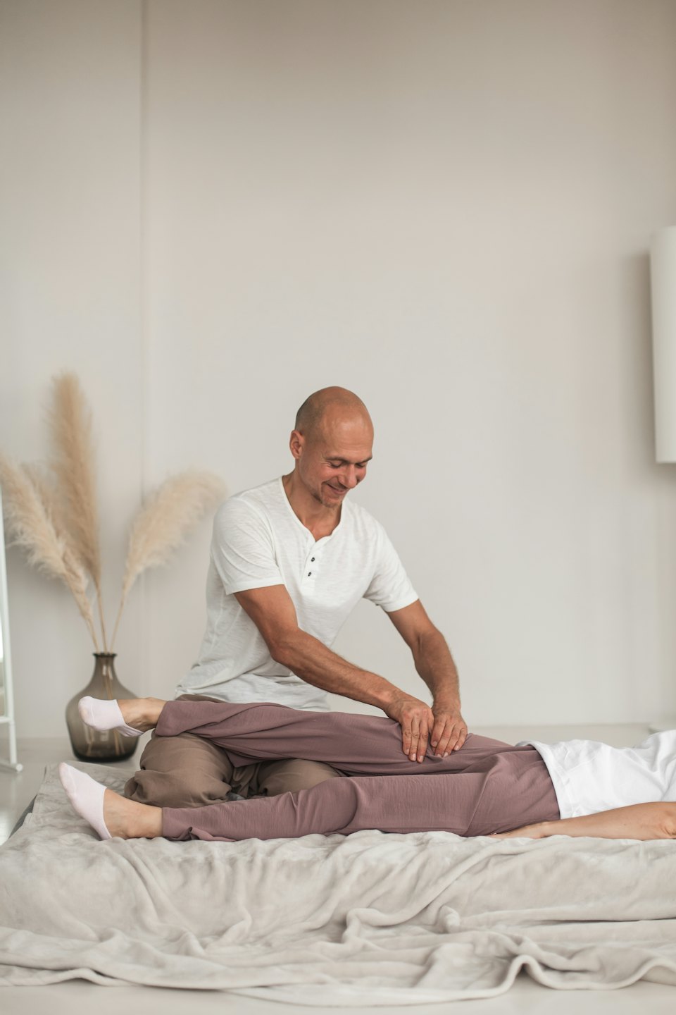 Masseur performs leg treatment on client lying on a mat.
